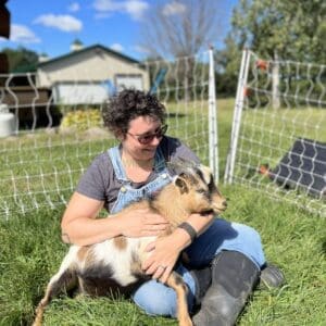 Woman sitting on lawn holding a bucking goat